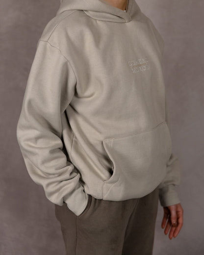 The Malla Hoodie in Natural Stone, three-quarter front, worn by a 5ft 6 model in size Small