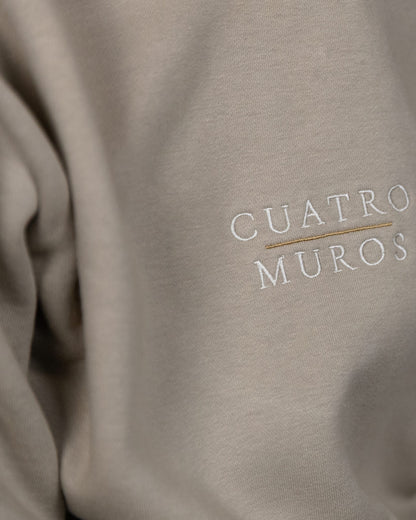 The Malla Hoodie in Natural Stone, close-up of the stacked wordmark embroidered in Oat Milk with a Desert Sand rule