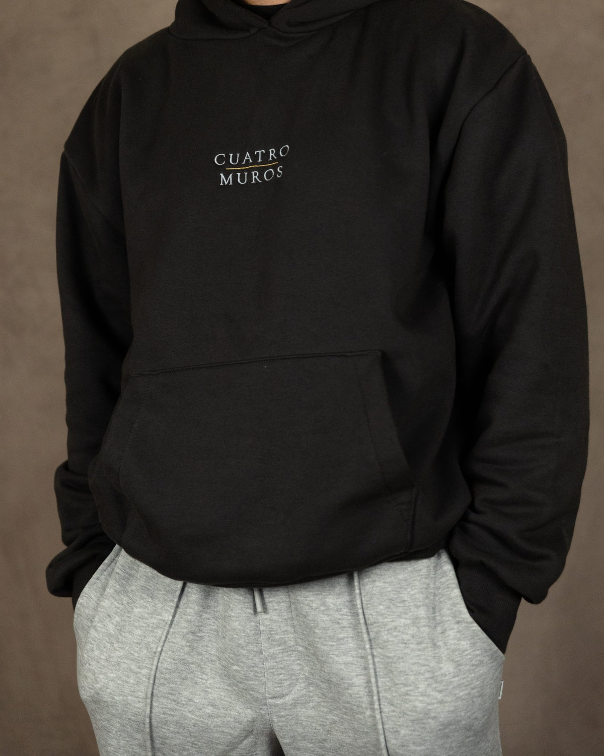 The Malla Hoodie in Solid Charcoal, front, the stacked wordmark embroidered at the centre chest, worn by a 6ft model in size Large