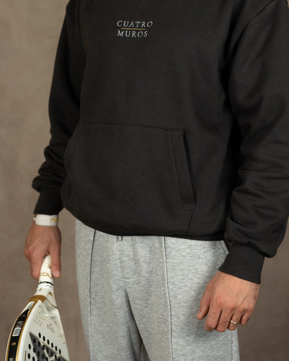 The Malla Hoodie in Solid Charcoal, front with a padel racket, worn by a 6ft model in size Large
