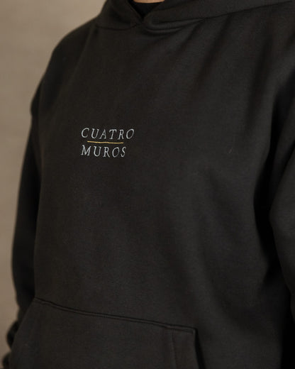 The Malla Hoodie in Solid Charcoal, close-up of the stacked wordmark embroidered in Oat Milk with a Desert Sand rule