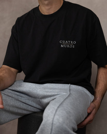 The Muro Tee in Faded Black, seated, worn by a 6ft model in size Large